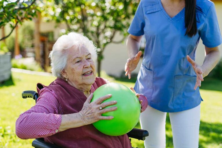 Residents and staff walk through a bright assisted living hallway with handrails, call buttons, and clear pathways.