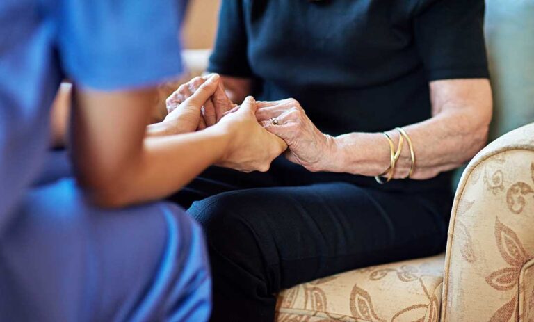 Older adult smiling with a family member during a quiet visit in a bright assisted living room.